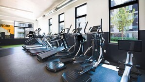 A gym with treadmills, stationary bikes, and a large window with a view of buildings.
