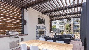 An outdoor patio with a wooden table, white chairs, a grill, a built-in oven, and a seating area. - Landing | Incredible 2BD, Clubhouse, Pool (Herriman)
