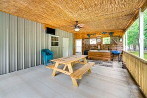 Una cabaña rústica con una mesa de madera y bancos, una zona de cocina y un amplio ventanal con vistas a la vegetación.