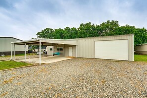 A single-story building with a covered patio, a garage door, and a gravel driveway. - Cozy Lake Texoma Getaway- Boat Parking-Fishing station-Family Retreat-Big Patio (Kingston)