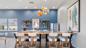 A modern dining area with a wooden table and chairs, pendant lights, and a kitchen in the background.