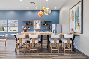 A modern dining area with a wooden table and chairs, pendant lights, and a kitchen in the background. - Landing | Incredible 1BD, Gym, Clubhouse (Richland)