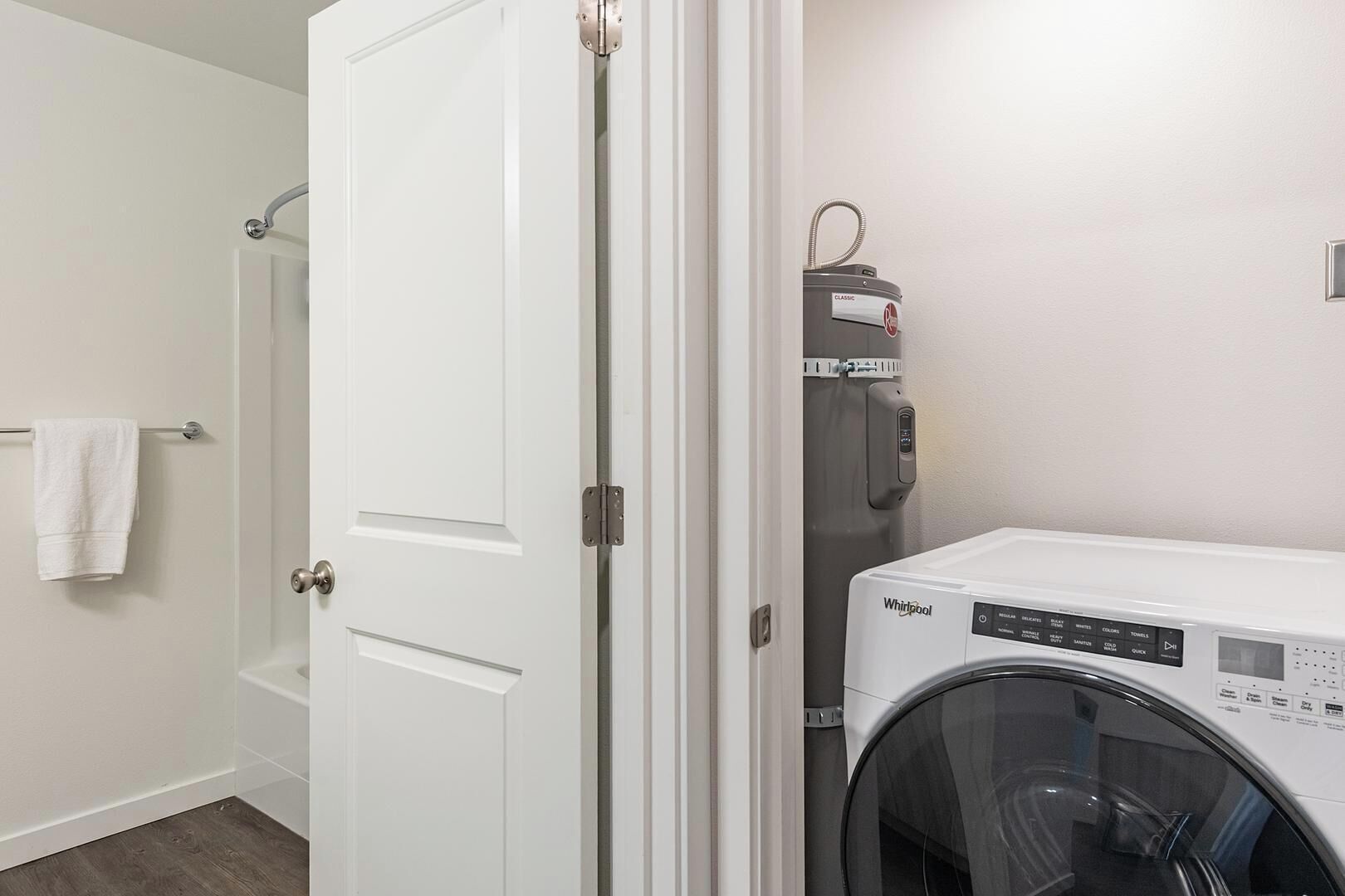 Una sala de lavandería con lavadora y secadora Whirlpool, una puerta blanca y un perchero para toallas.