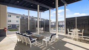 Patio esterno con mobili bianchi, un braciere e vista su edifici residenziali.