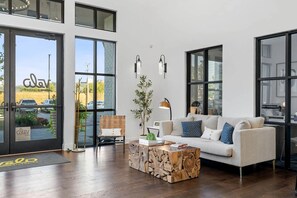 Ein modernes Wohnzimmer mit Sofa, Couchtisch und Sessel. Große Fenster bieten einen Blick ins Freie.