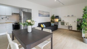 Een moderne keuken met witte kasten, een donker houten eettafel en een grijze bank in de woonkamer.