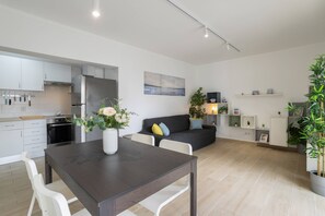 Eine moderne Küche mit weißen Schränken, einem dunklen Holztisch im Essbereich und einem grauen Sofa im Wohnbereich.