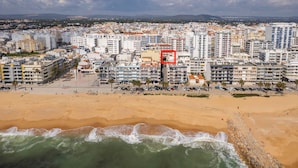 Luchtbeeld van een kustplaats met een strand, gebouwen en een rode vierkant die een specifiek gebied markeert.