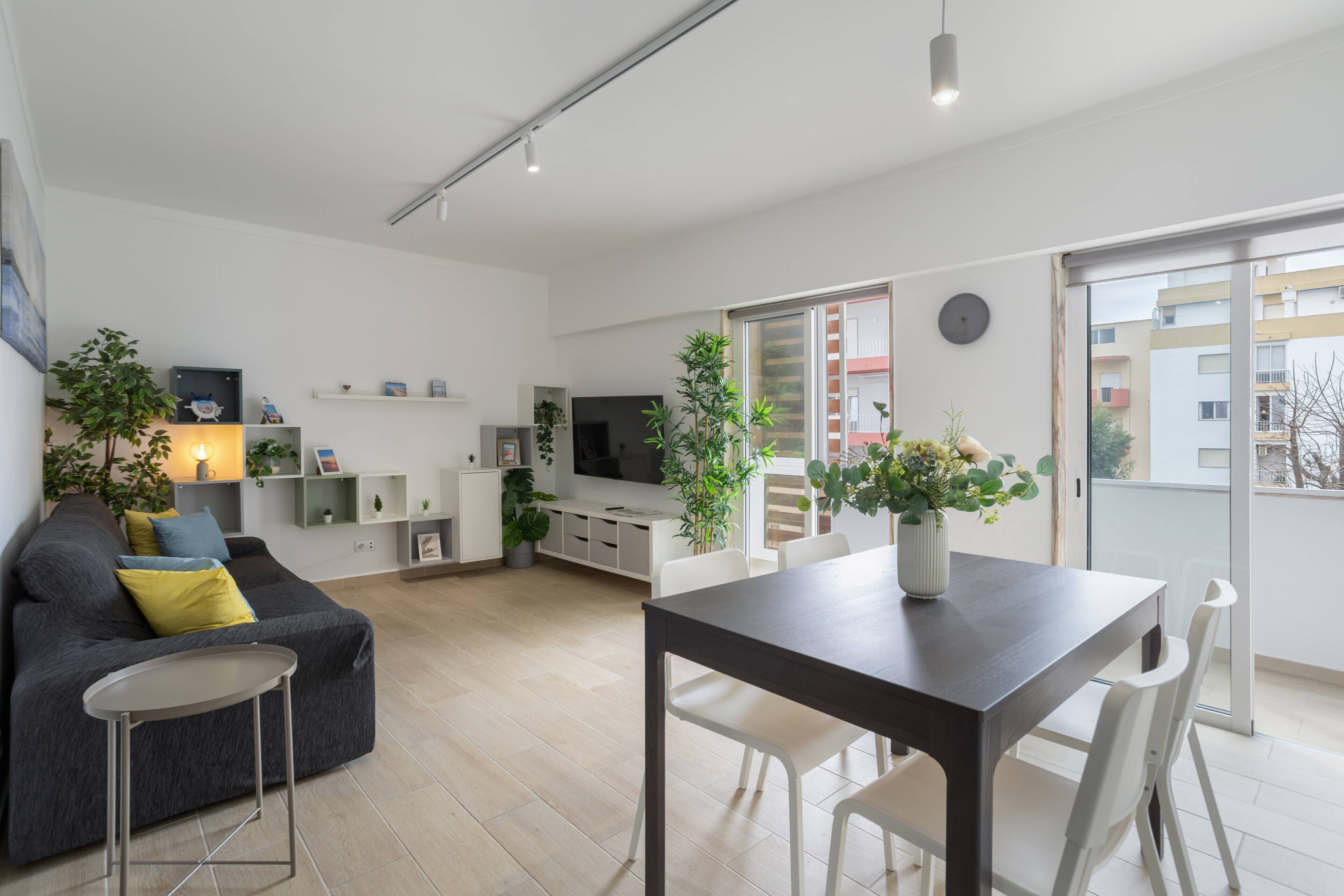 A modern living room with a sofa, dining table, chairs, a TV, and potted plants.