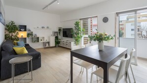 Een moderne woonkamer met een bank, een eettafel, stoelen, een televisie en potplanten.