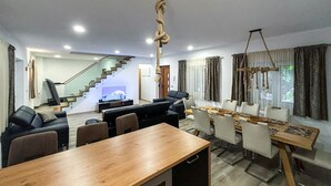 A modern living room with a wooden dining table, black sofas, and a staircase leading to an upper floor.