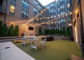 An outdoor patio with a brick wall, string lights, and seating. - Landing | Modern 1BD, Gym (Columbus)