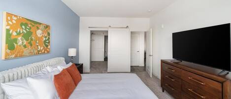 A bedroom with a bed, a TV, a dresser, a painting, and a closet.