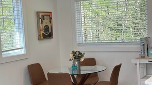 Un comedor con una mesa redonda de cristal, sillas marrones, un tapete tejido y colorido, y un jarrón con flores.