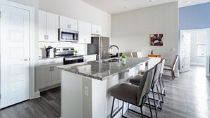 Eine moderne Küche mit weißen Schränken, Edelstahlgeräten, einer Granit Arbeitsplatte und einer Bar mit Barhocker.