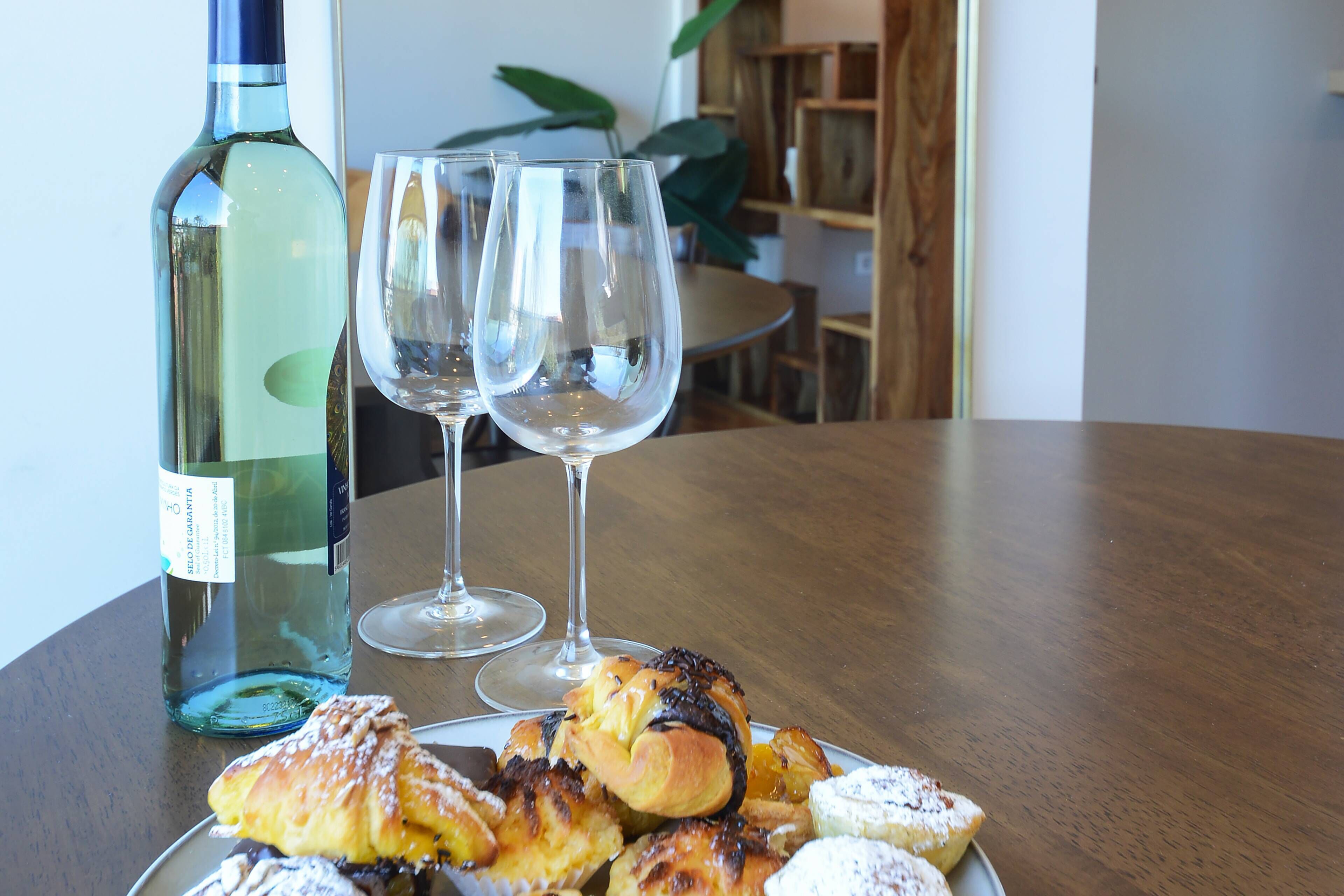 A table with pastries, a bottle of wine, and two wine glasses.