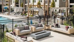 A poolside area with outdoor seating and a view of a multi-story building. - Landing | Chic 1BD, Yoga Studio, Gym (Summerville)