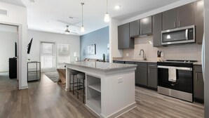 A modern kitchen with a central island, stainless steel appliances, and a blue accent wall. - Landing | Chic 1BD, Yoga Studio, Gym (Summerville)