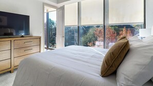 Ein Schlafzimmer mit einem großen Bett, einem Fernseher auf einer Holzkommode und einem Fenster mit Blick auf Bäume.
