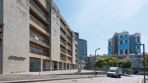 Ein mehrgeschossiges Gebäude mit Tiefgarage, ein modernes Gebäude mit blauen Akzenten, und eine Straße mit einem parkenden Lastwagen.