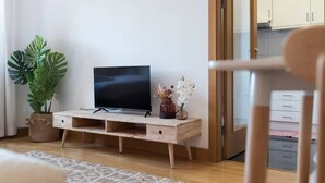 Ein Wohnzimmer mit einem Holz-Fernsehschrank, einem Blumentopf, einer Vase mit Blumen und einem gemusterten Teppich.