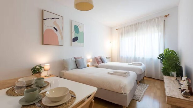 Ein Hotelzimmer mit zwei Betten, einem Esstisch gedeckt mit Tellern und Tassen, einer Lampe und einer Pflanze.