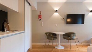 A modern kitchen with a built-in sink, a dining area with two chairs and a small table, and a mounted flat-screen TV. - VIVA Santa Catarina  Serviced Apartments -2 (Porto)
