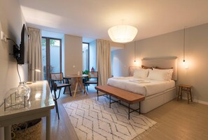 Una habitación de hotel moderna con una cama, mesita de noche, lámpara y vistas al exterior.
