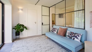 Una habitación con un sofá azul claro, un espejo grande, una planta en maceta y una puerta blanca.