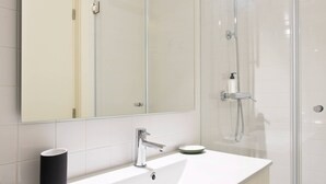 Een moderne badkamer met een grote spiegel, een wit wastafelmeubel en een douchecabine met glazen wanden.
