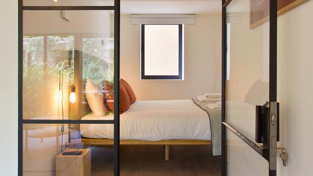 Een moderne slaapkamer met een glazen scheiding, een bed, een nachtkastje en een raam.