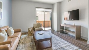 Un soggiorno con divano, tavolino, televisore e una porta scorrevole in vetro che dà su un balcone.