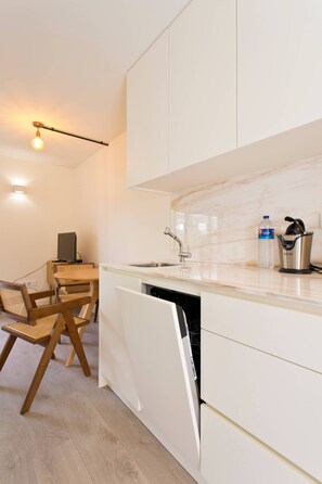 A modern kitchen with white cabinetry, a dishwasher, a sink, a water dispenser, and a coffee maker. - VIVA Travessa dos Campos Serviced Apartments C (Porto)