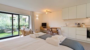 Habitación de hotel moderna con una cama grande, un escritorio, un televisor y vistas a un jardín a través de amplias ventanas.