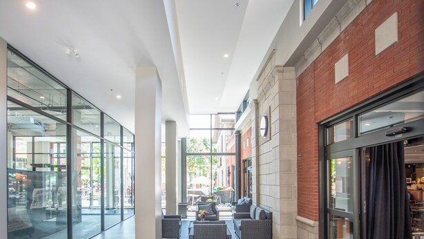 A modern hotel lobby with glass walls, a seating area with sofas, a wooden table, and a brick wall. - Belmont Properties Short-Term Rentals (Gatineau)