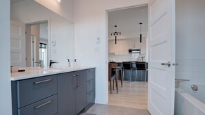 A modern kitchen with grey cabinets, a white countertop, and a dining area with a bar stool. - Belmont Properties Short-Term Rentals (Gatineau)