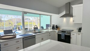 Una cucina moderna con mobili bianchi, una stufa in acciaio inossidabile e un'ampia finestra con vista su una piscina.