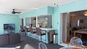 A room with a TV, bar area, seating, and a view through a window.