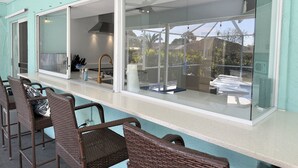 Una cucina con piano cottura a gas, lavandino e ventilatore a soffitto. All'esterno dell'area cucina, ci sono sedie in vimini e un tavolo.