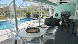 Un'area esterna riparata con piscina, sedie trasparenti, un tavolo e una ventola a soffitto.