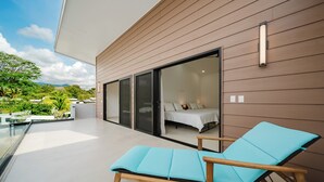 Une chambre moderne dotée d’un lit, d’un balcon avec un fauteuil de relaxation et offrant une vue sur la verdure et les montagnes.