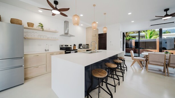Une cuisine moderne dotée d’un îlot central, de tabourets de bar, de ventilateurs de plafond et offrant une vue sur l’extérieur.