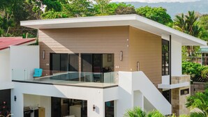 Une maison moderne à deux étages, dotée d’un balcon, d’une piscine et offrant une vue sur une végétation luxuriante.