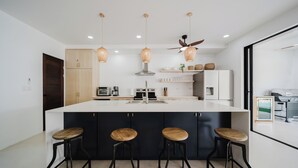 Une cuisine moderne dotée d’un îlot central, de tabourets de bar, de luminaires suspendus et d’un ventilateur de plafond.