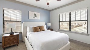 Ein Schlafzimmer mit einem Bett, zwei Nachttischen, einem Deckenventilator und Fenstern mit Jalousien.