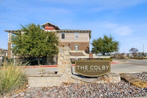 A residential building with a stone entrance and a sign that reads 'THE COLBY AT CASTLE HILLS.' - Landing | Spectacular 3BD, Clubhouse (Carrollton)