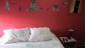 A bed with a white quilt, a small bedside table with a lamp, and a wall with Eiffel Tower and other Parisian-themed decorations. - B5 Furnished cottage near downtown Puerto Montt (Puerto Montt)