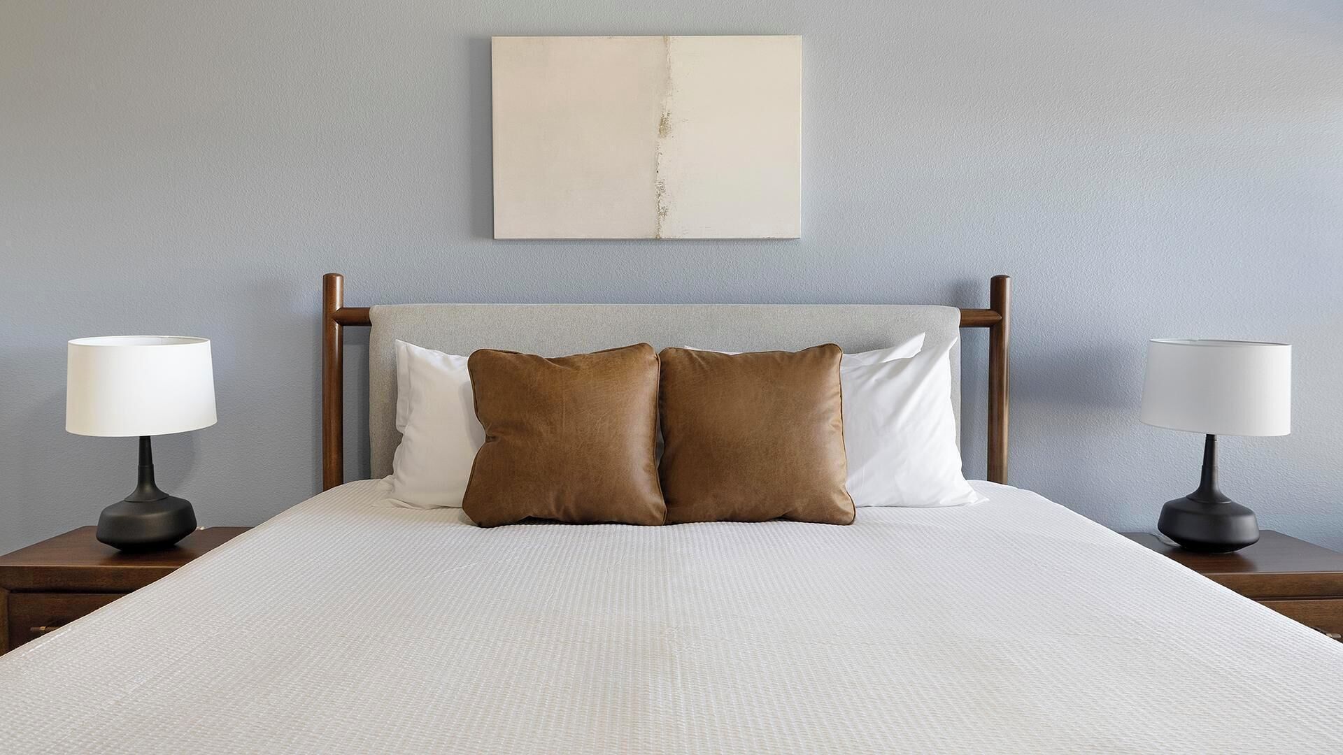 A bed with a white bedspread, two brown pillows, and a wooden headboard. There are two bedside lamps on wooden nightstands.