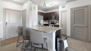 A modern kitchen with granite countertops, stainless steel appliances, and a central island with bar stools. - Landing | Beautiful 2BD, Clubhouse (Carrollton)