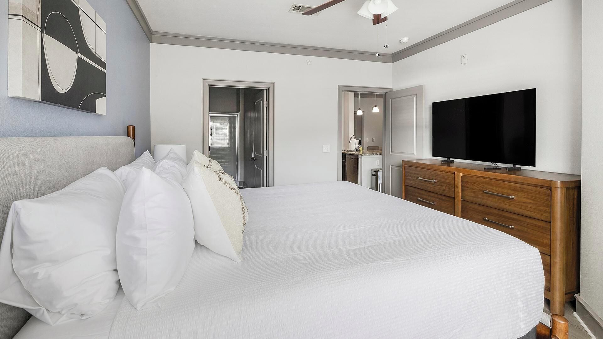 Ein Schlafzimmer mit einem großen Bett, einem Fernseher, einer Holzkommode und einem Gemälde an der Wand.